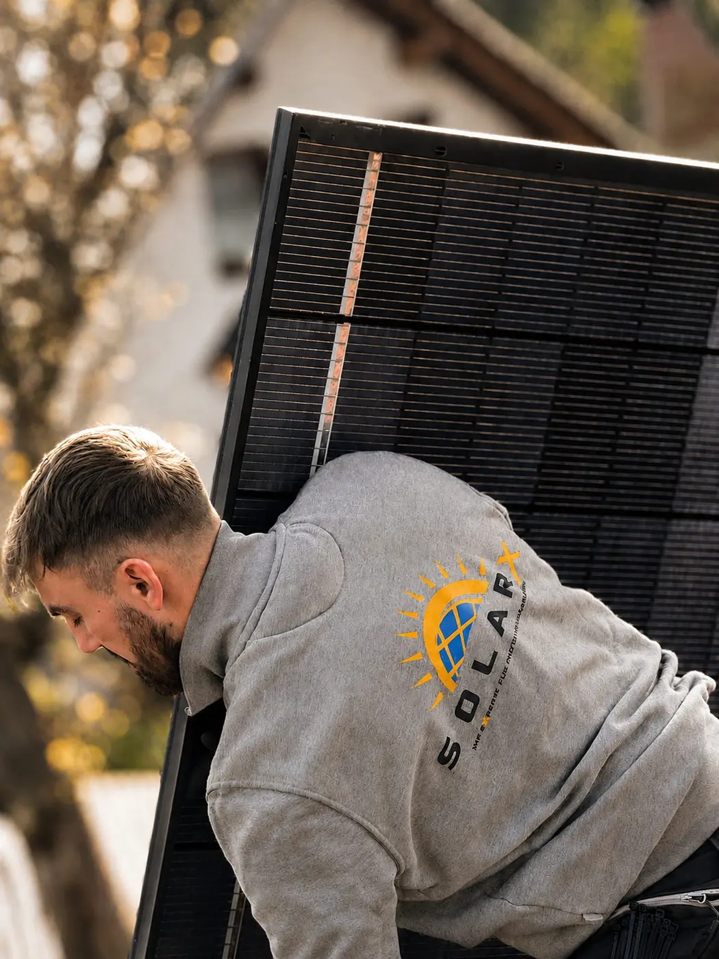 SolarX – Monteur trägt ein Solarmodul zur Dachmontage SolarX-Monteur transportiert ein schwarzes Solarmodul zur Dachmontage