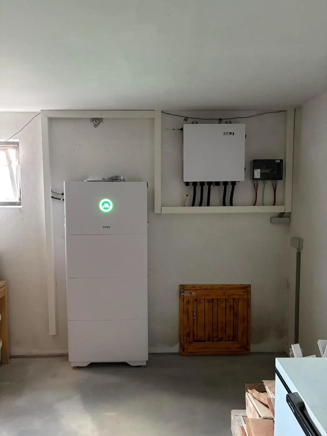 Photovoltaik-Referenz SolarX – Speicher, Wechselrichter und Zähler SolarX Referenz: Speicher an der Wand eines hellen Kellerraums, rechts daneben Wechselrichter und Zähler