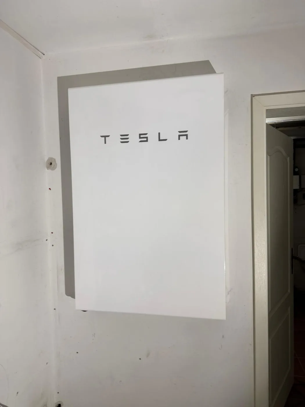 Photovoltaik-Referenz SolarX – Tesla Powerwall neben einem Durchgang SolarX Referenz: Tesla Powerwall an einer weißen Wand neben einem Durchgang