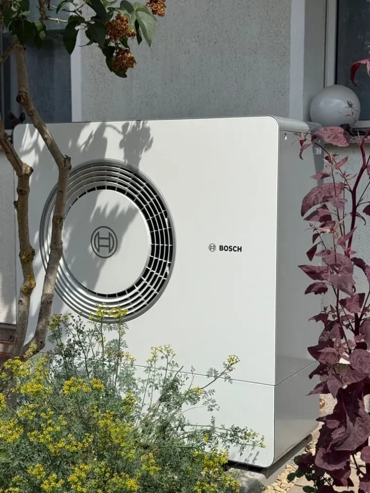 HeatX – Bosch Wärmepumpen-Außeneinheit an einer Hauswand Bosch-Außeneinheit mit Ventilator an einer Hauswand im Garten